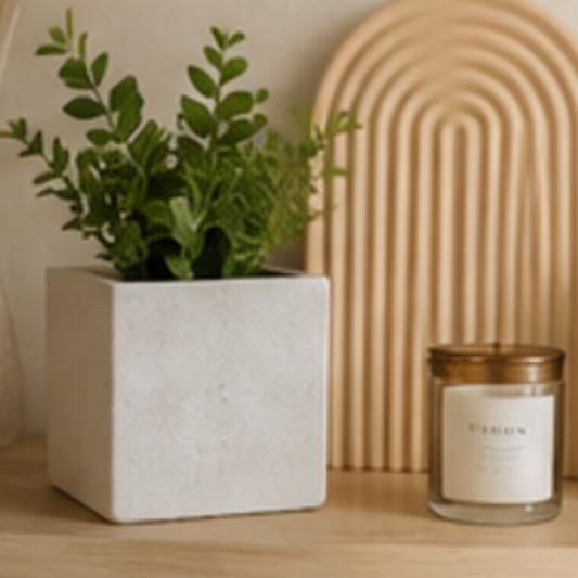 Candle and potted plant on a wooden surface with a decorative arch in the background