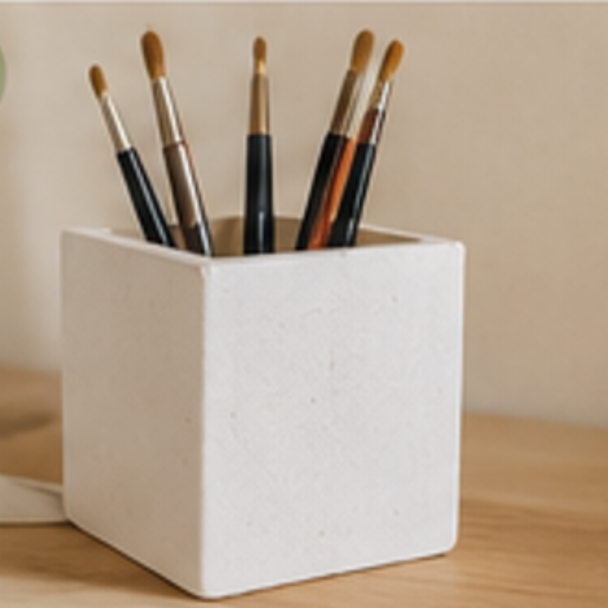 Set of paintbrushes in a white ceramic holder on a wooden surface.